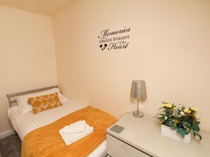Een net opgemaakt bed met een geborreld deken, een bedlamp, een klein plantje en een wanddecoratie.