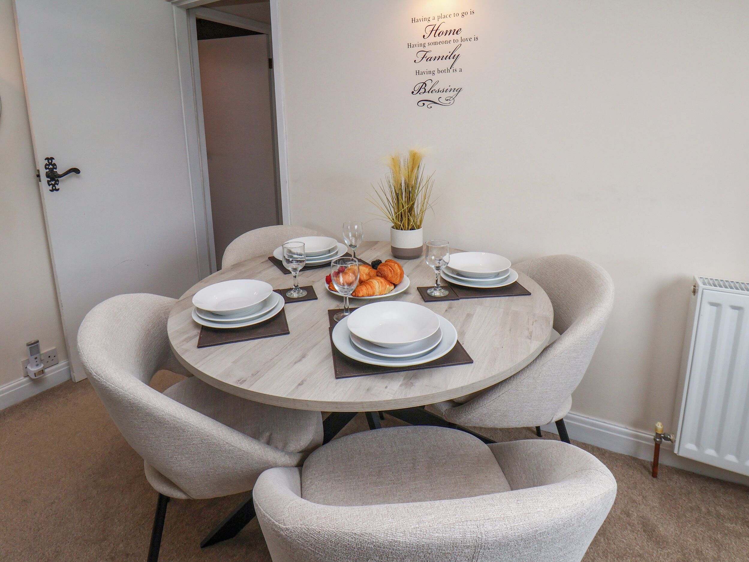 A dining area with a round table set for four, chairs, plates, glasses, and a small plant.