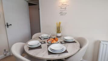 A dining area with a round table set for four, chairs, plates, glasses, and a small plant.