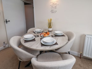 Comedor con una mesa redonda dispuesta para cuatro personas, sillas, platos, vasos y una planta pequeña.