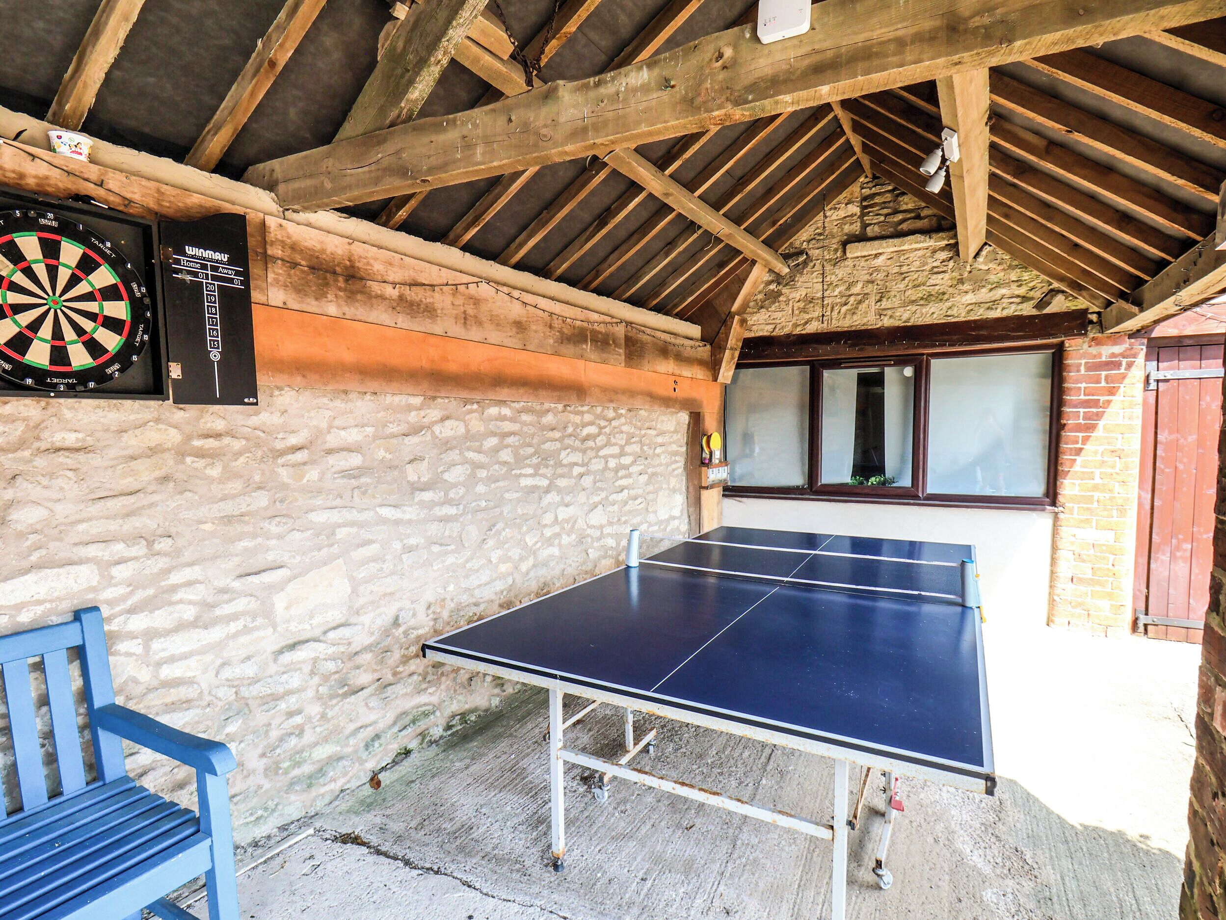 A ping pong table in a rustic room with a dartboard and a blue chair.