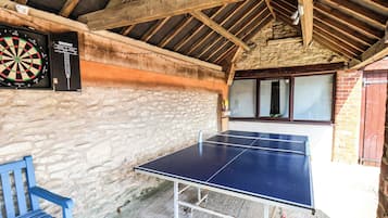 A ping pong table in a rustic room with a dartboard and a blue chair.