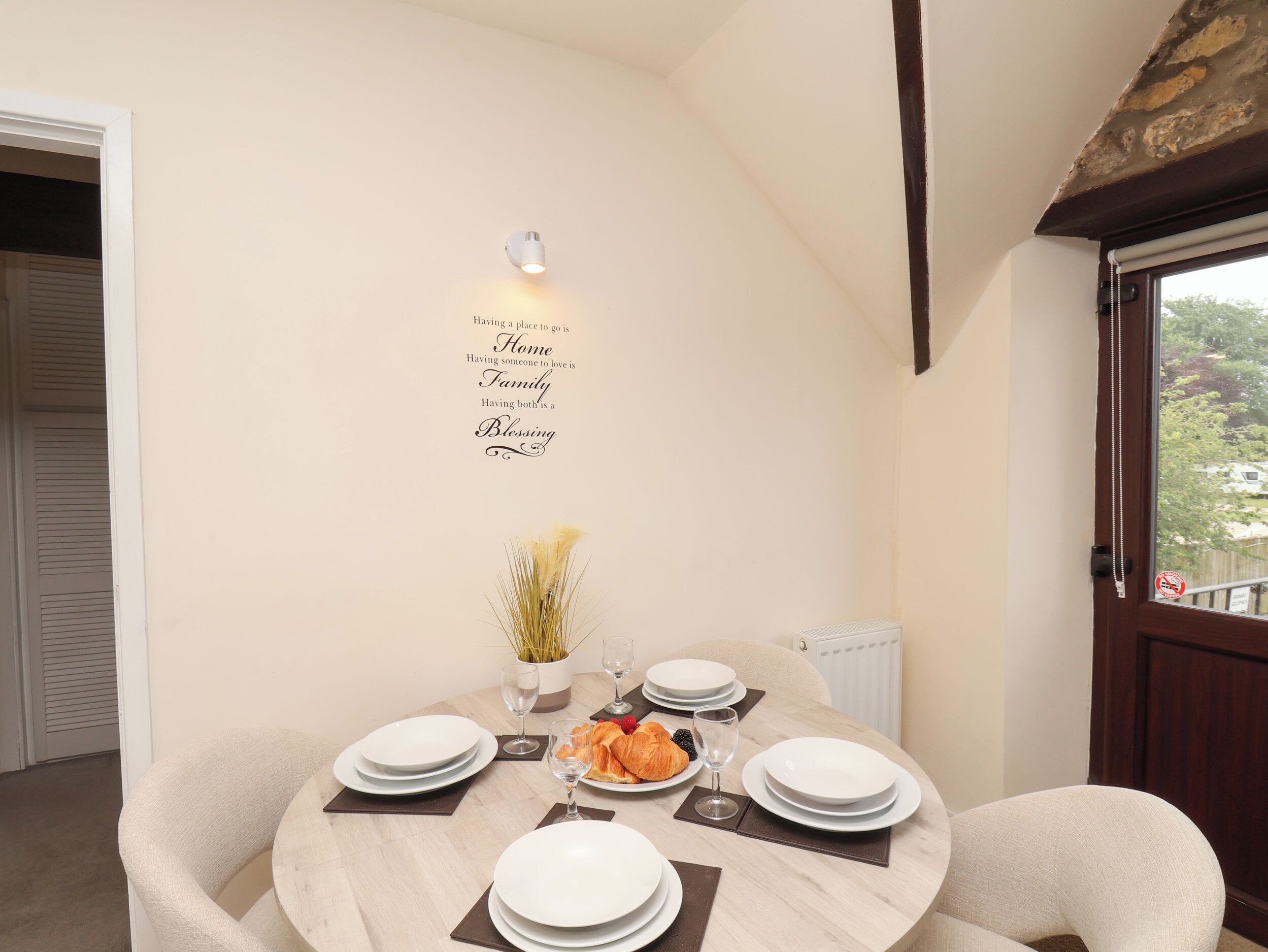 A dining area with a round table set for four, a wall-mounted light, and a decorative sign.
