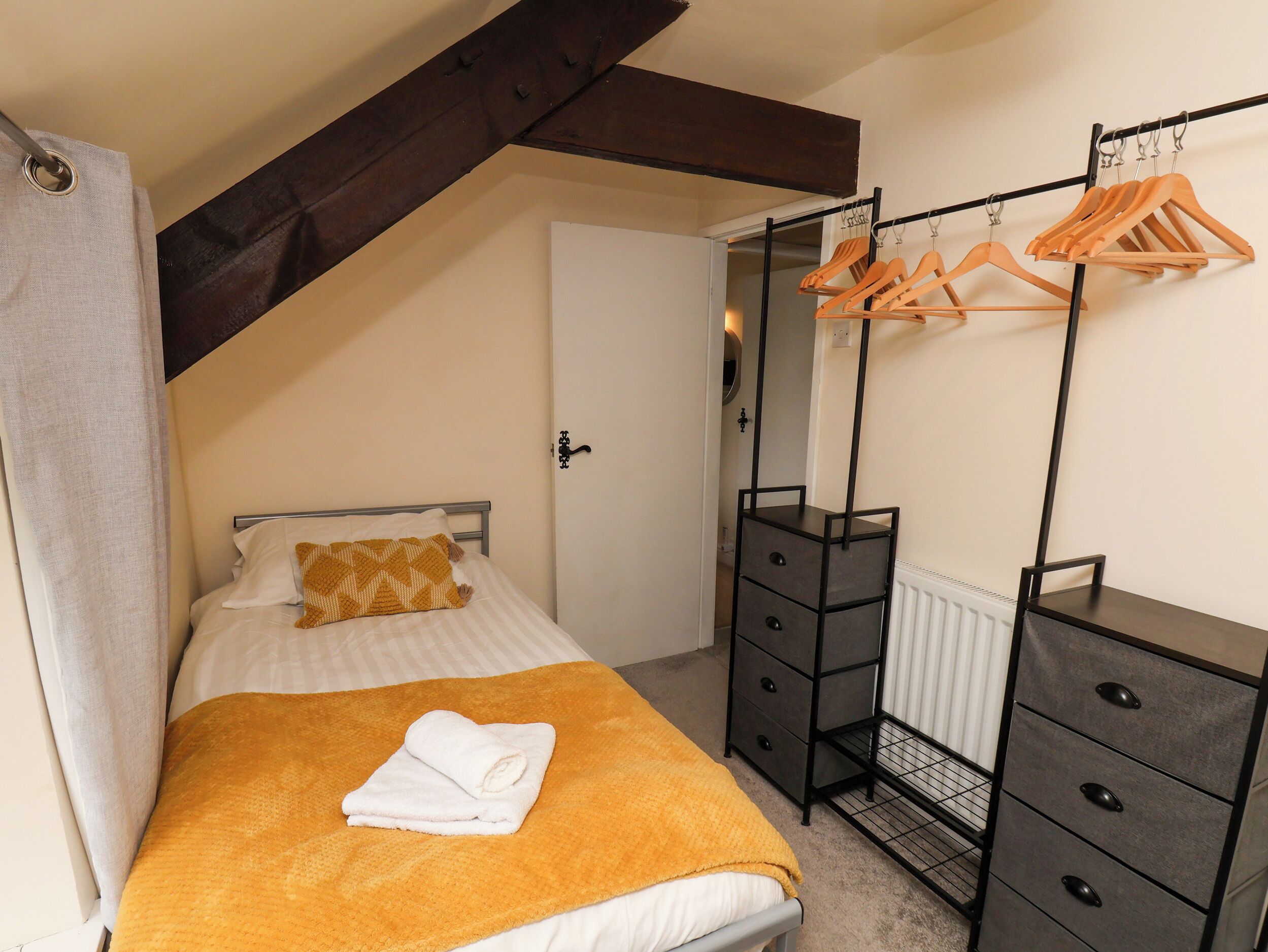 A bedroom with a bed, a wooden bench, a radiator, and a clothing rack.