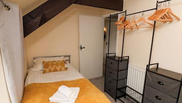 A bedroom with a bed, a wooden bench, a radiator, and a clothing rack.