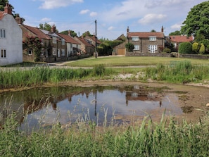 A rural setting with traditional stone houses, a small pond, and surrounding greenery. - Granary (Pickering)