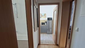 Un couloir étroit au plancher en bois, avec un banc et une vue sur un coin cuisine comprenant un réfrigérateur et des placards.