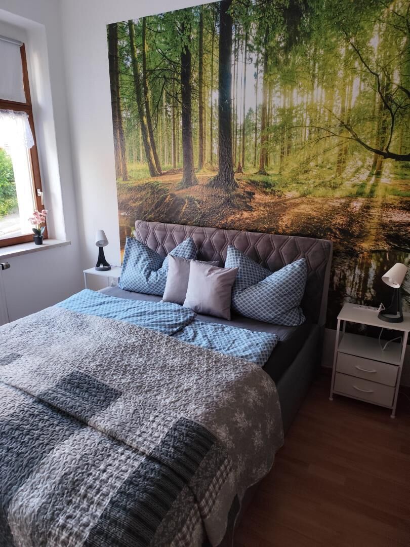 Une chambre à coucher avec un grand lit, une tête de lit, une table de chevet, une lampe et une fenêtre.
