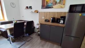 Une cuisine moderne équipée d’un réfrigérateur, d’une machine à café et d’un four à micro-ondes. On y trouve une table à manger avec des chaises, ainsi qu’une horloge au mur.