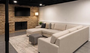 A modern living room with a sectional sofa, a fireplace, and a flat-screen TV mounted on a brick wall. - Charming newly remodeled 3-bedroom house in Itasca with all the latest amenities (Itasca)
