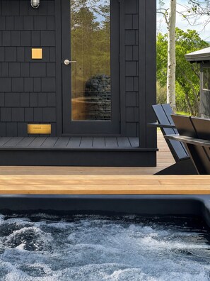 Ein moderner Außenbereich mit Whirlpool, Holzterrasse und Glastür, vor einer Steinsäule.