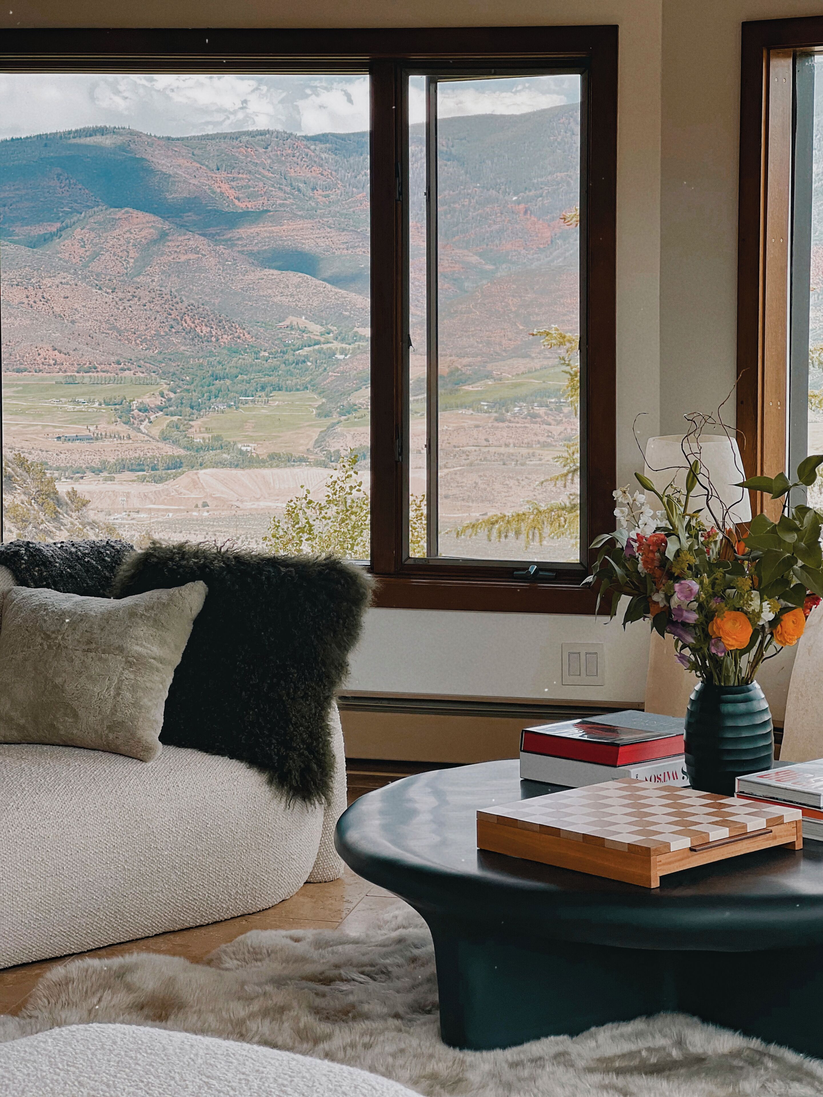 Una habitación con un ventanal grande, un sofá, una mesa de centro y un florero con flores.