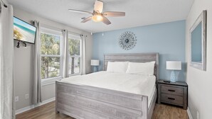 A bedroom with a bed, ceiling fan, bedside lamps, a TV, and a decorative wall piece. - Beachside Villas 1023 (Santa Rosa Beach)