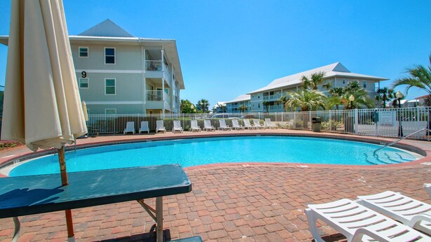 A swimming pool with lounge chairs and umbrellas, surrounded by a brick walkway and a white fence. - Beachside Villas 1023 (Santa Rosa Beach)
