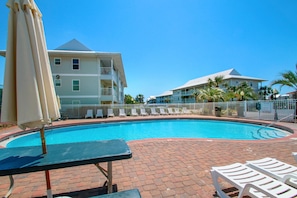 A swimming pool with lounge chairs and umbrellas, surrounded by a brick patio and a white fence. - Beachside Villas 1023 (Santa Rosa Beach)