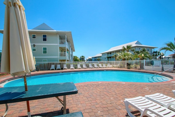 A swimming pool with lounge chairs and umbrellas, surrounded by a brick walkway and a fence. - Beachside Villas 1023 (Santa Rosa Beach)