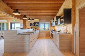 Una cocina moderna con armarios de madera, una isla central, iluminación colgante y vistas a través de las ventanas.
