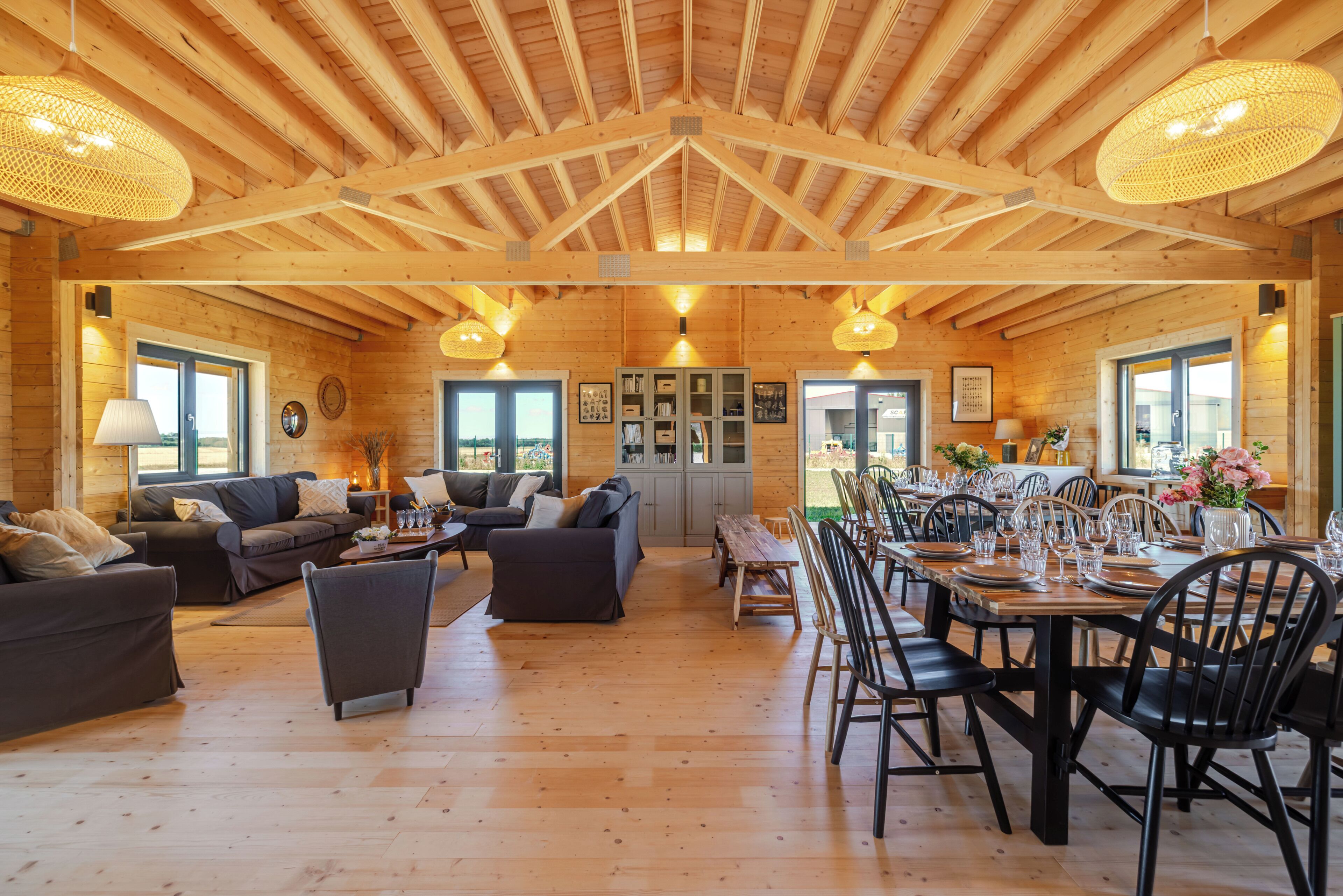 A spacious wooden interior with a high ceiling, multiple seating areas, and a dining setup.