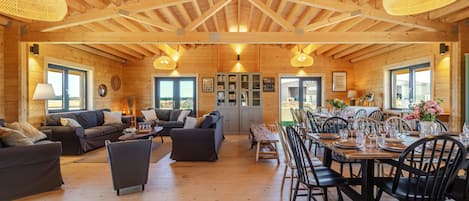 A spacious wooden interior with a high ceiling, multiple seating areas, and a dining setup.