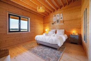 Ein Zimmer mit Holzboden, einem Bett, Nachttischlampen, einem Fenster und gerahmten Bildern an der Wand.