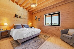 Un dormitori de cabana de fusta amb un llit, làmpades de nit, una finestra i un sofà.