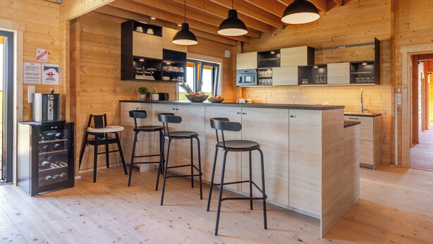 Ein Holzinnenraum mit einer Küchenzeile, inklusive Bar, Hockern und Kühlschrank.