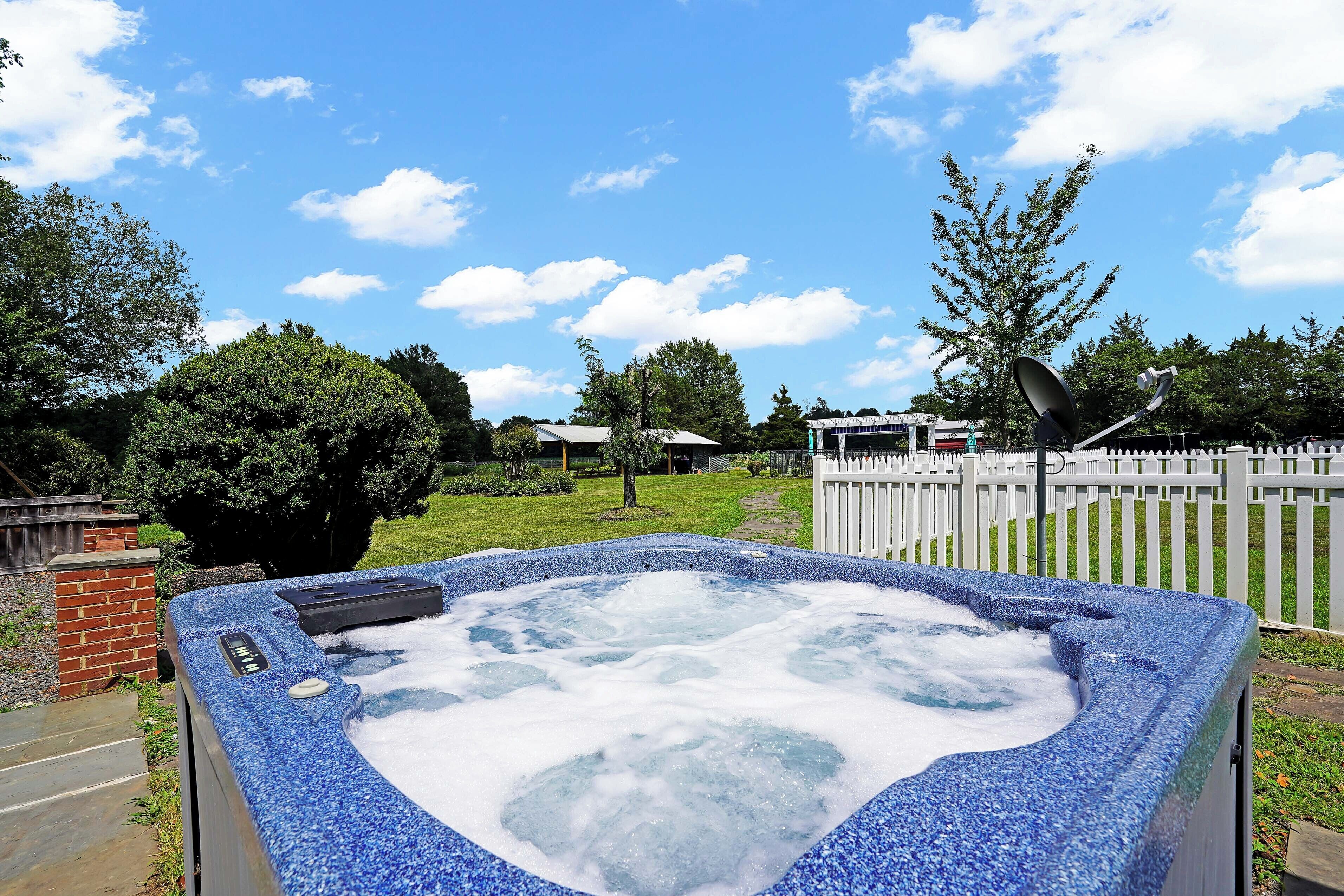 A hot tub with a stone exterior, surrounded by a white fence, a brick structure, and a tree.