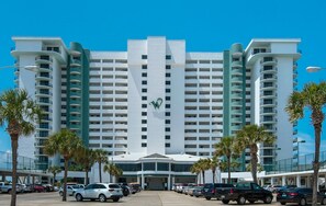 Ein großes, mehrgeschossiges Hotel mit einem auffälligen 'W'-Logo an der Fassade, das einen zentralen Eingang und einen Parkplatz mit mehreren Autos bietet.