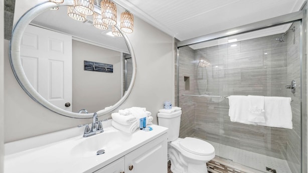 A modern bathroom with a glass shower, a round mirror, and a white sink. - Watercrest 1006 (Panama City Beach)