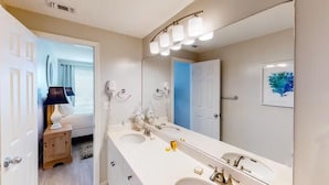 Une salle de bain avec un double vasque, un grand miroir et un luminaire placé au-dessus du miroir.