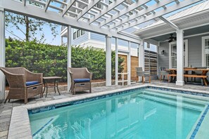 Ein Poolbereich mit einer Pergola, Korbmöbeln und Blick auf ein Wohngebäude.