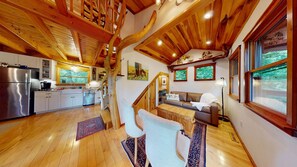 Ein rustikales Blockhaus-Interieur mit Küche, Essbereich und Wohnzimmer mit Sofa und Sesseln.