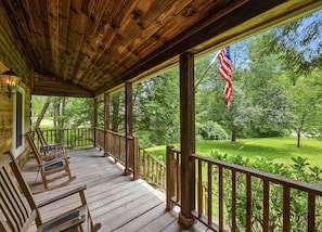 Une véranda en bois avec une balustrade, des fauteuils à bascule et un drapeau américain.