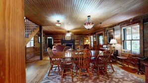 L’intérieur d’une cabane en rondins comprend un coin repas, une cheminée et de grandes fenêtres.