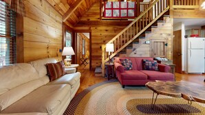L’intérieur d’un chalet confortable, avec un canapé, un divan rouge, une lampe et un escalier.