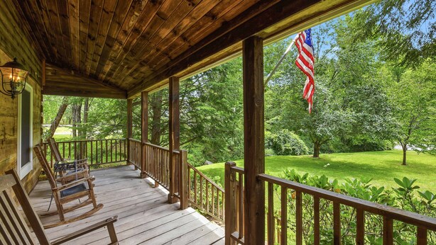 Une véranda en bois avec une balustrade, des fauteuils à bascule et un drapeau américain.