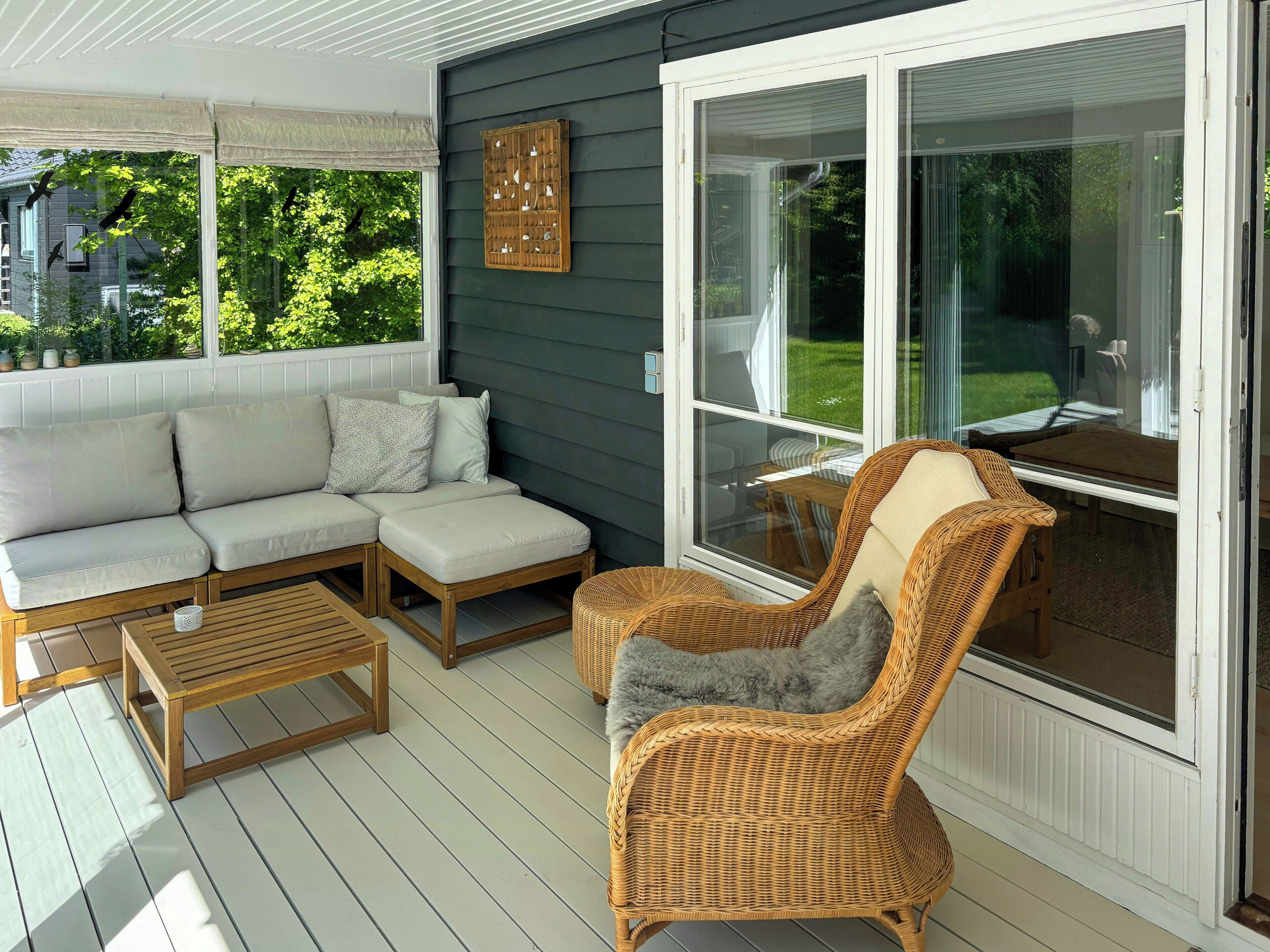 A covered porch with a sofa, wicker chairs, and a table.
