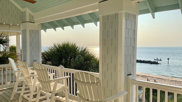Een overdekt terras met witte stoelen, een plafondventilator en uitzicht op de oceaan.