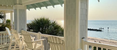 A covered outdoor seating area with white chairs, a ceiling fan, and a view of the ocean.