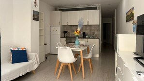 Una cocina moderna con armarios blancos, una mesa de comedor con sillas y un televisor sobre un mueble.