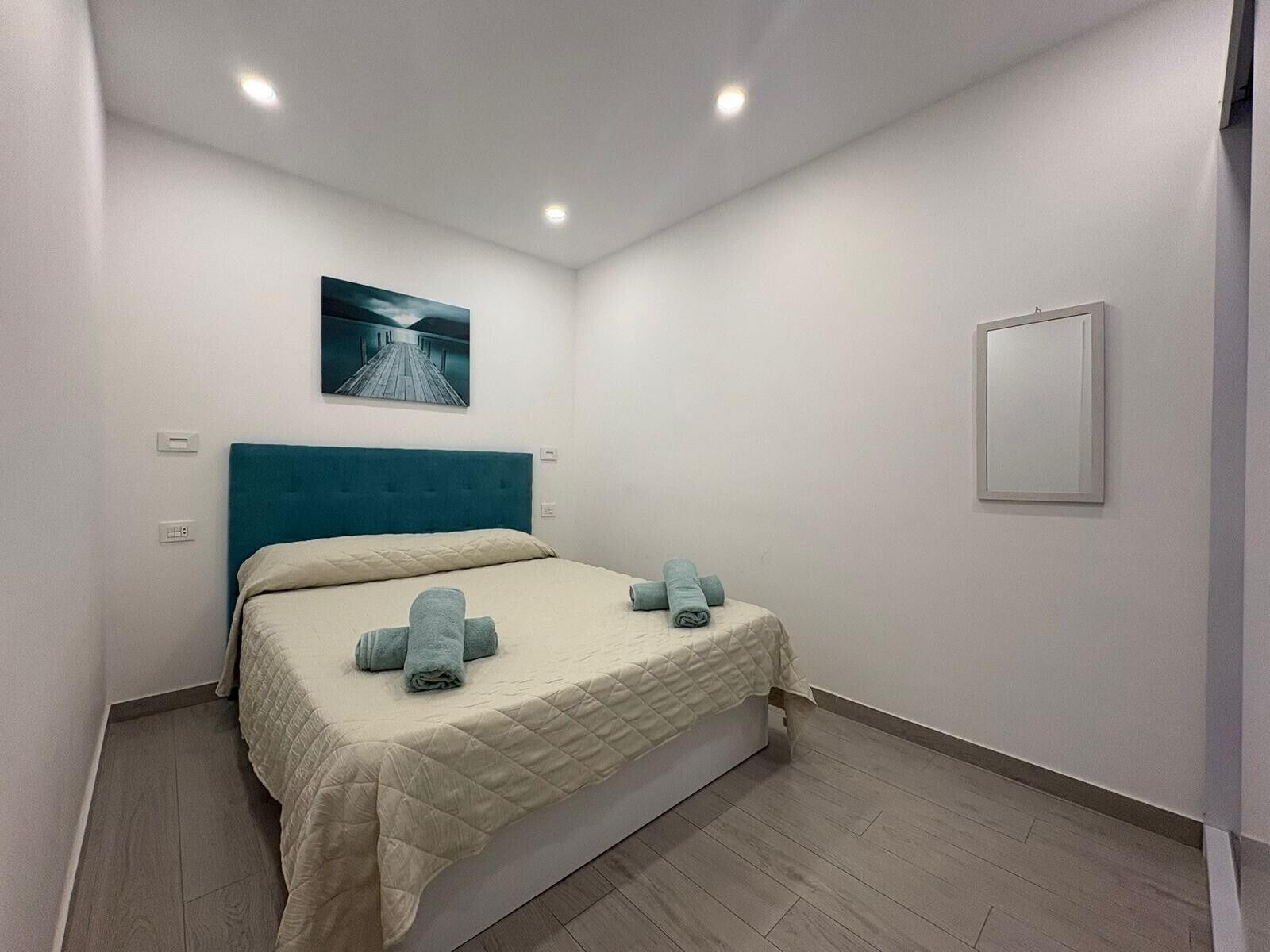Ein Schlafzimmer mit Bett, einem Kopfteil, einem Wandbild und einem Schminkspiegel am Nachttisch.