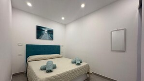 Un dormitorio con cama, cabecera, un cuadro colgado en la pared y un espejo en la mesita de noche.