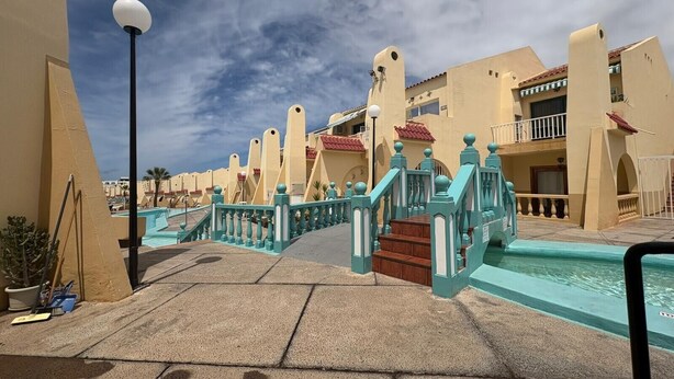 Un resort con piscina, barandales turquesa y cielo despejado.