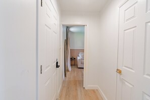 A hallway with white doors leading to a bedroom with a bed and a nightstand. - The Parkway Boutique Hotel by the Falls (Niagara Falls)