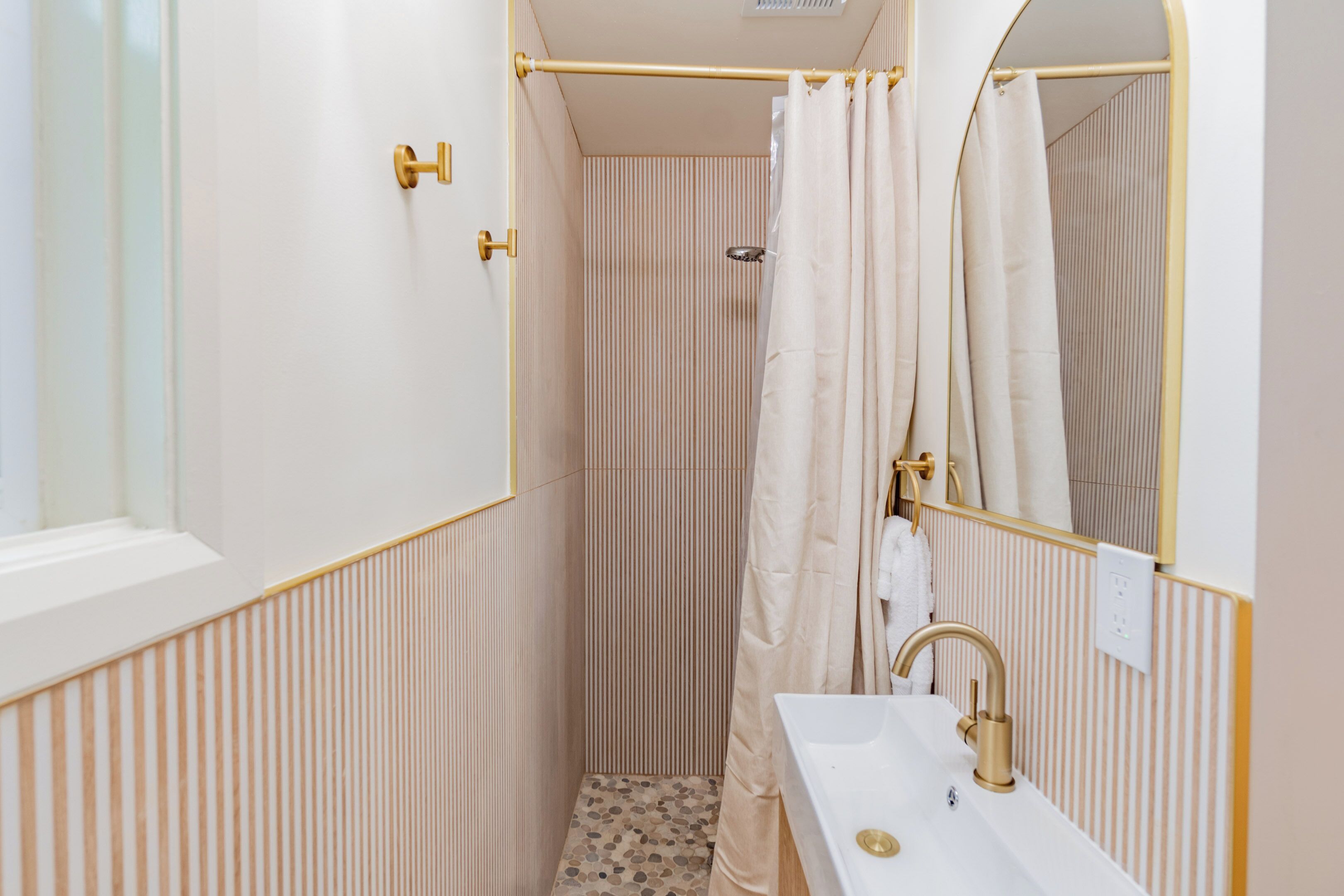 A bathroom with a shower, a sink with a gold faucet, and a mirror.