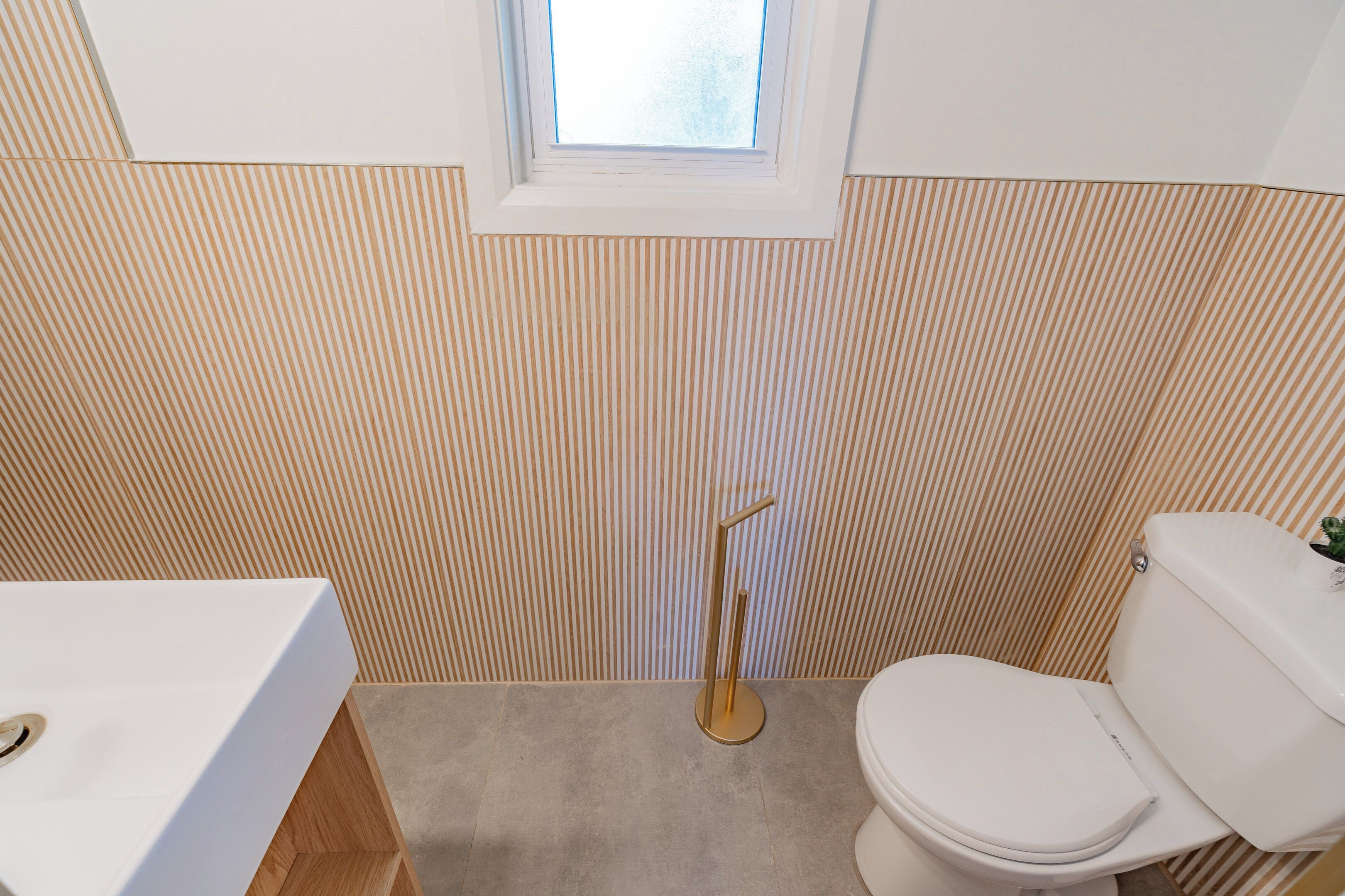 A bathroom with a striped wall, a window, a toilet, and a sink.