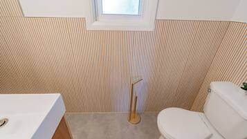 A bathroom with a striped wall, a window, a toilet, and a sink.