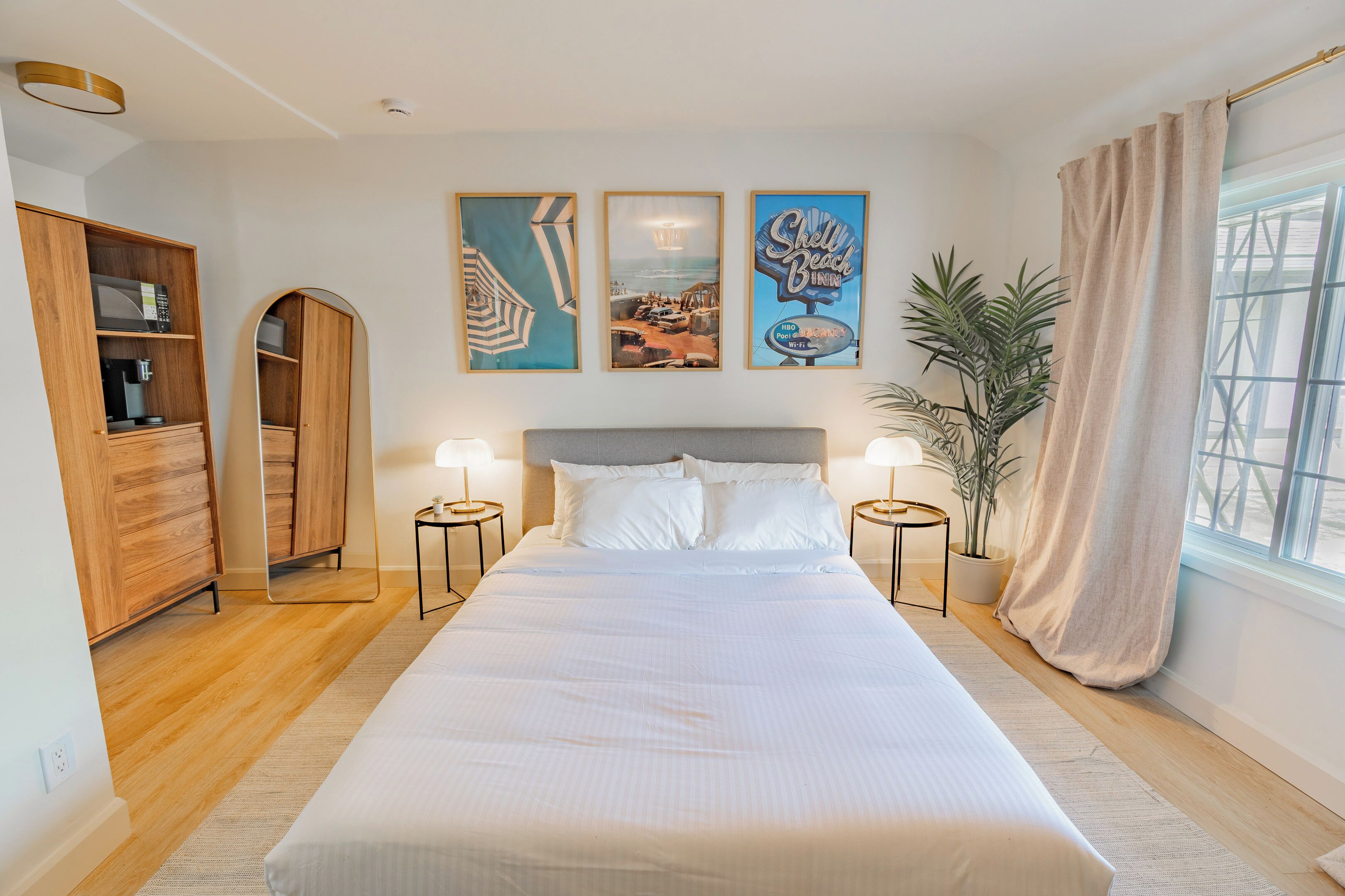Een slaapkamer met een groot bed, een houten kledingkast, twee nachtkastjes, een potplant en drie ingelijste foto's aan de muur.