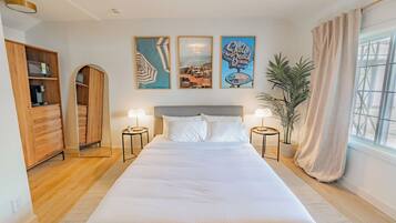 Een slaapkamer met een groot bed, een houten kledingkast, twee nachtkastjes, een potplant en drie ingelijste foto's aan de muur.