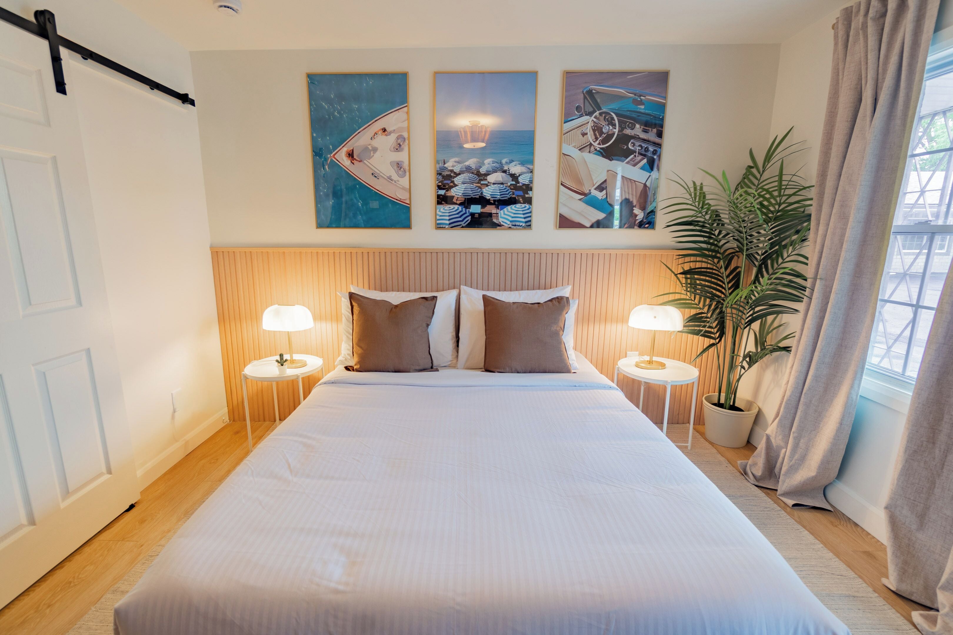 A hotel room with a large bed, two bedside tables with lamps, a potted plant, and three framed pictures on the wall.